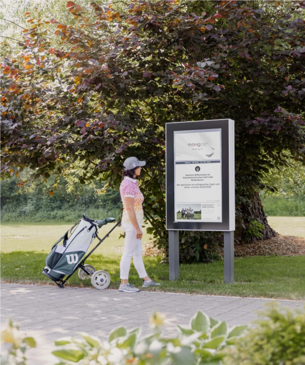 Frau schaut sich ein Infopanel auf einem Golfplatz an.