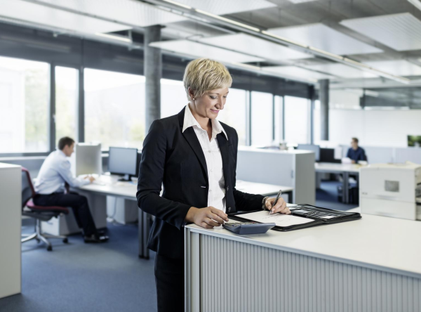 Mitarbeiterin die im Büro steht und Dokumente betrachtet